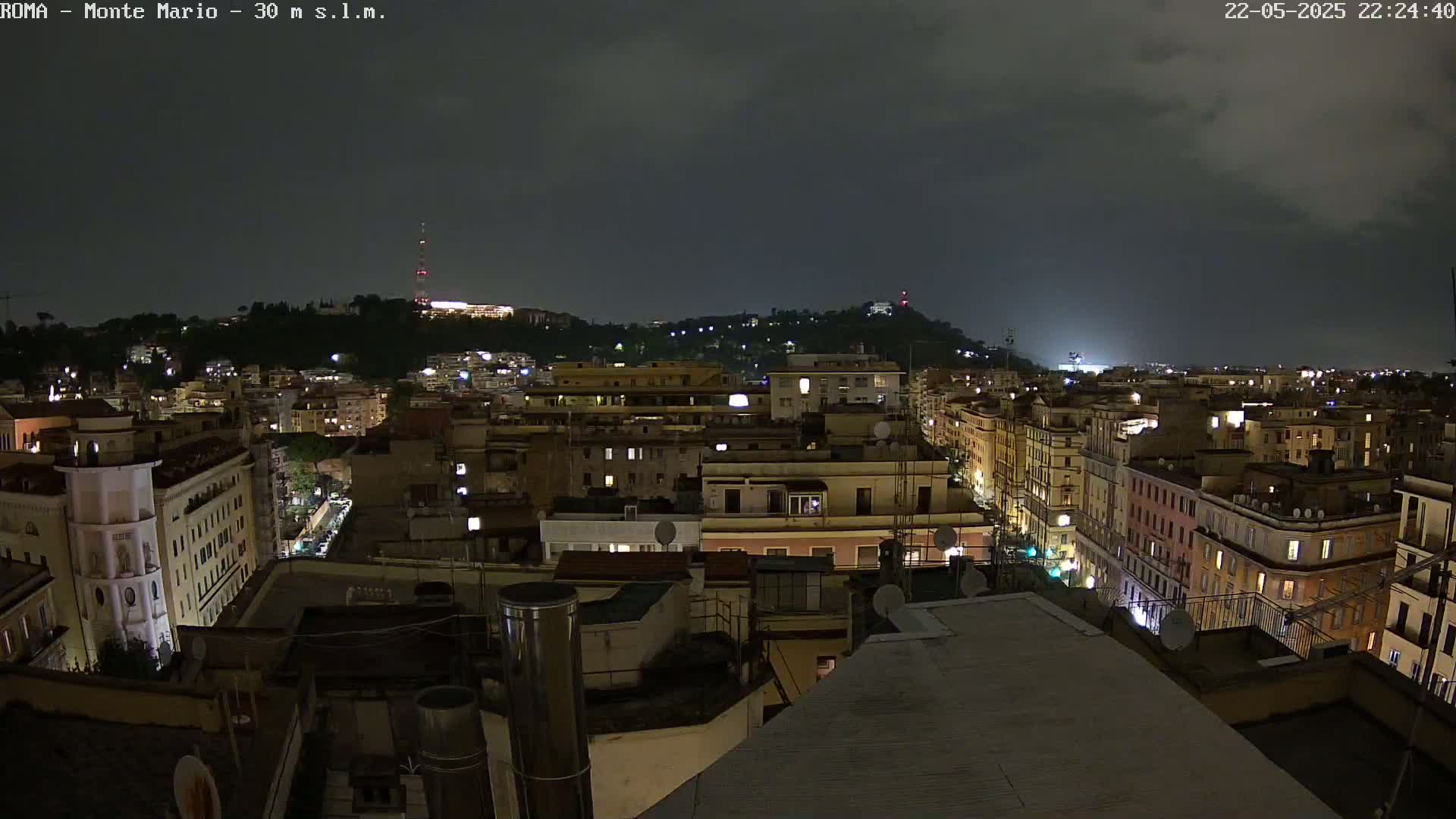 A nighttime view of a city with illuminated buildings under a dark, cloudy sky.