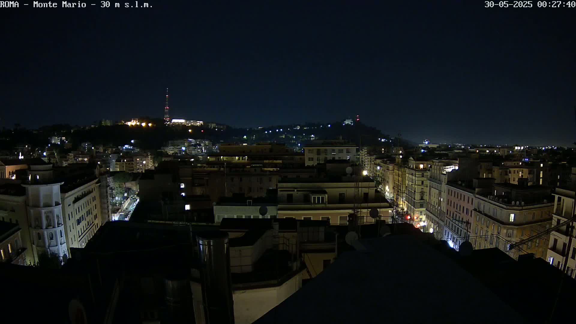 A nighttime, aerial view of a city with numerous buildings illuminated by lights under a clear, dark sky.