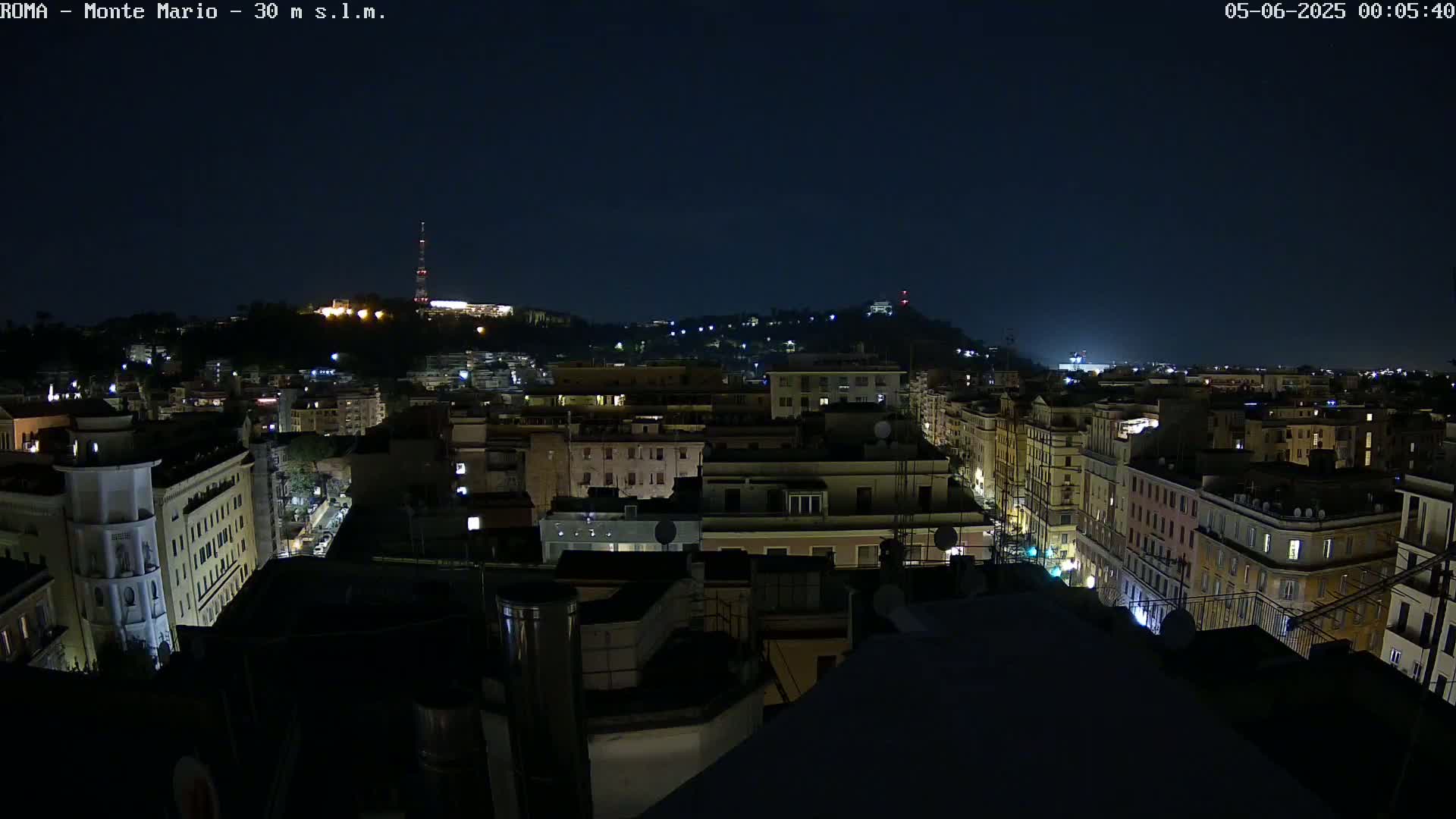 A nighttime view of a city, showing buildings illuminated with some lights on, under a dark, clear sky.