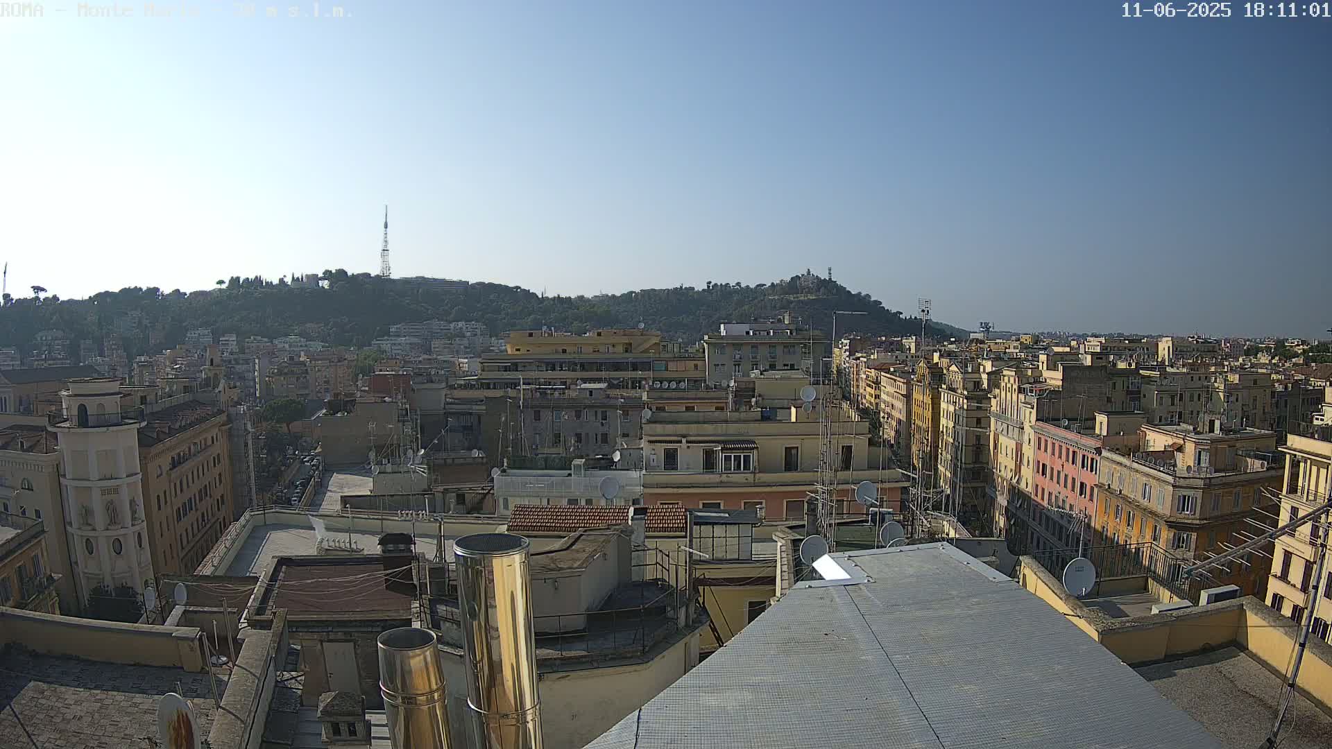 A high-angle view of a city on a clear, sunny day, showing numerous buildings and a hill in the distance.