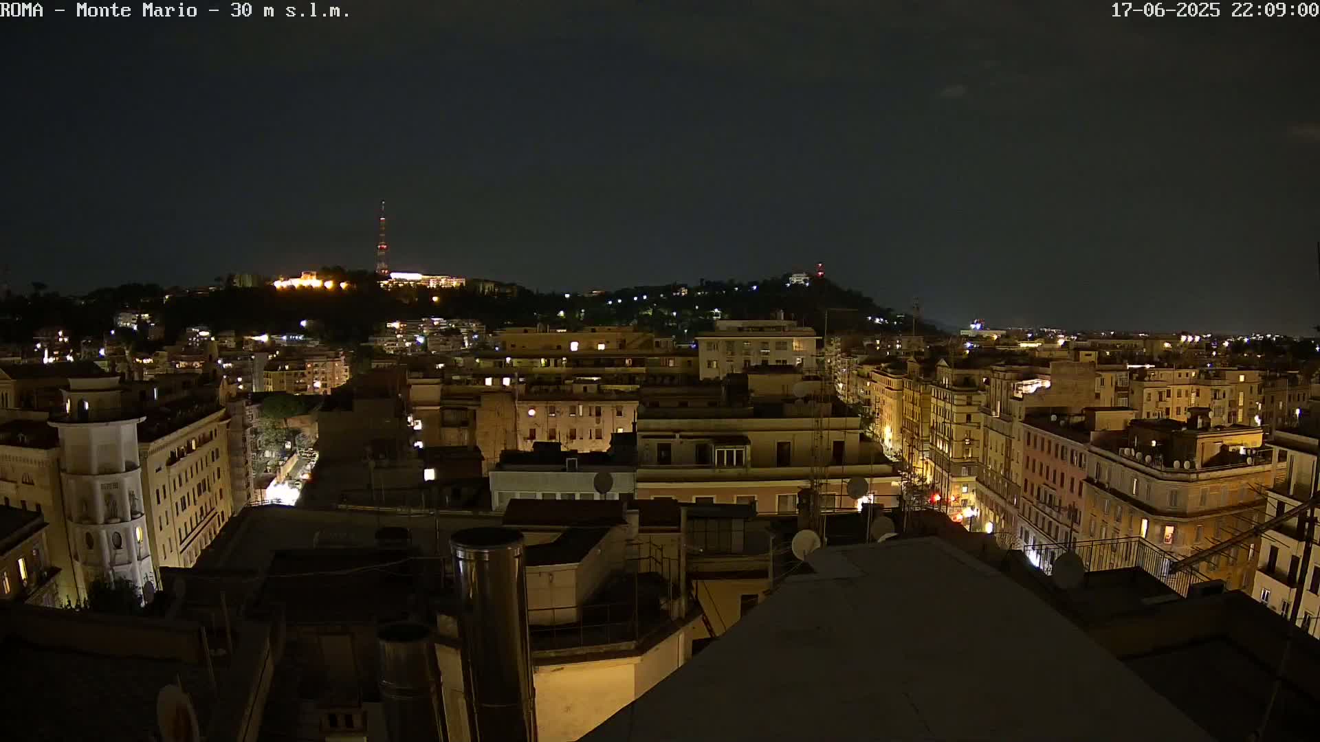 A nighttime view of a city with illuminated buildings stretching to a hilltop in the distance under a clear, dark sky.