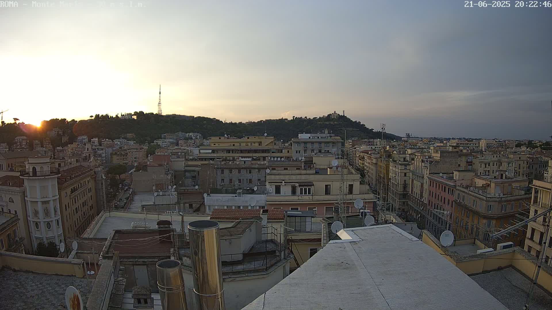 A sunset view over a dense cityscape of multi-story buildings, with a hill in the background.