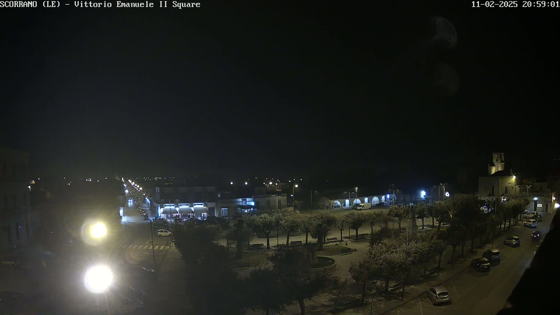 A nighttime, overhead view of a town square with trees, buildings, cars, and streetlights.