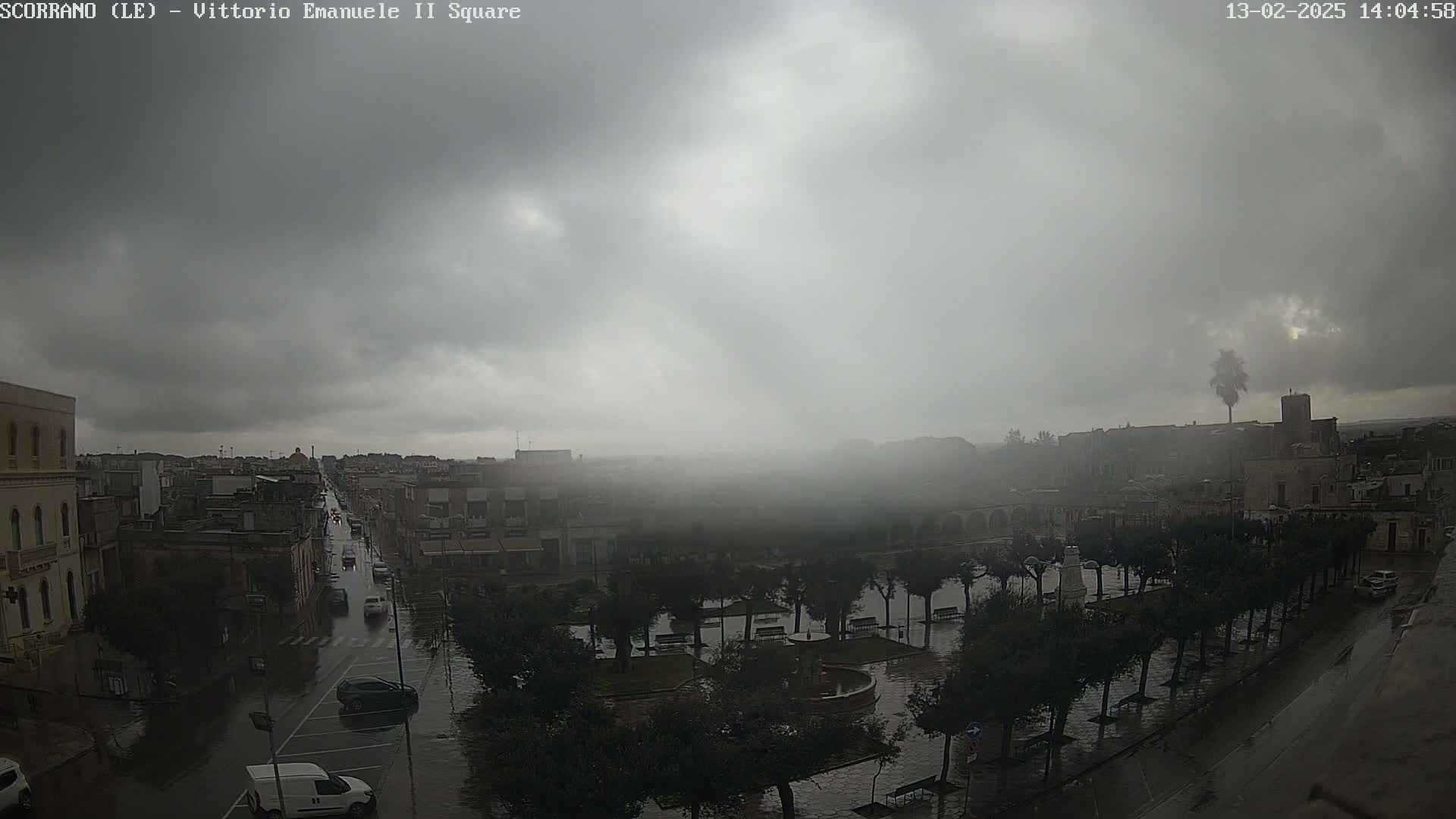 A town square and surrounding streets are shown under a heavily overcast sky during a light rain.