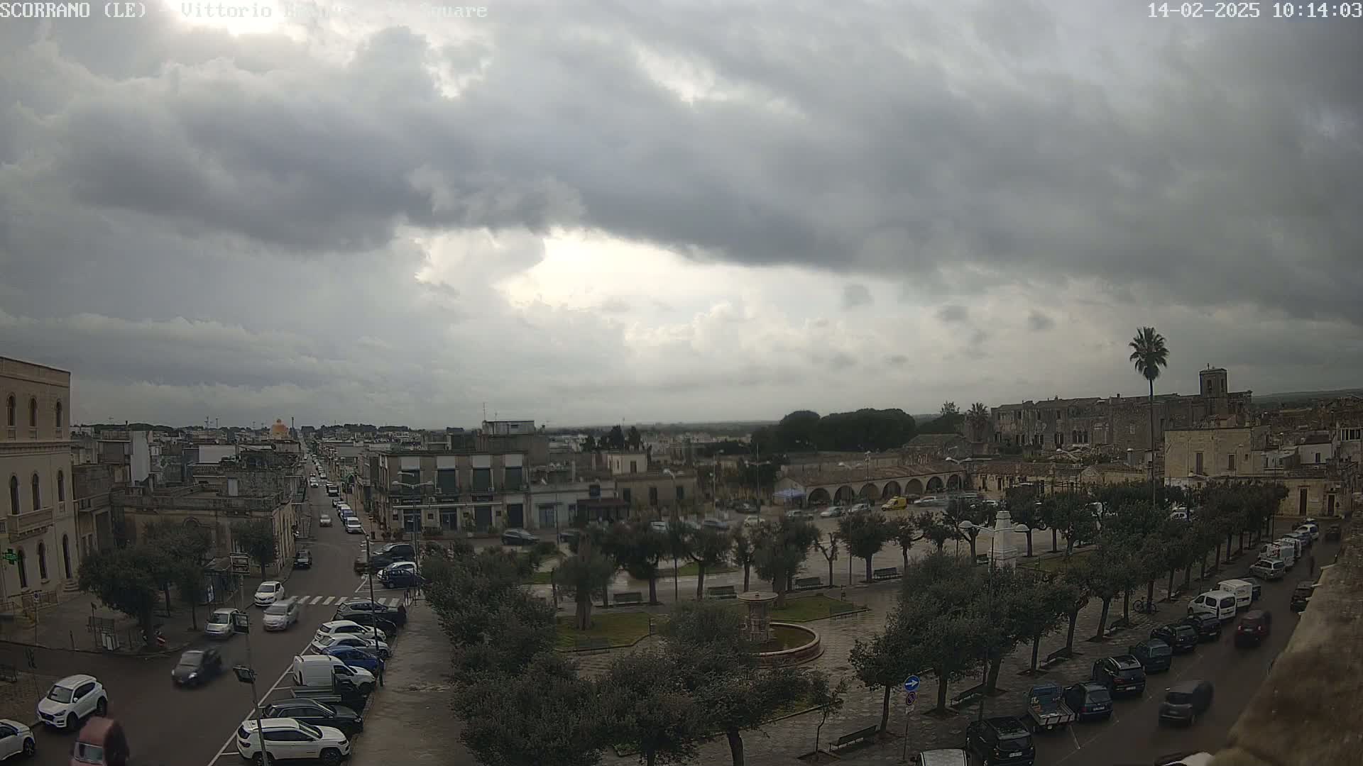 A town square with parked cars and a fountain is visible under a heavily overcast sky.