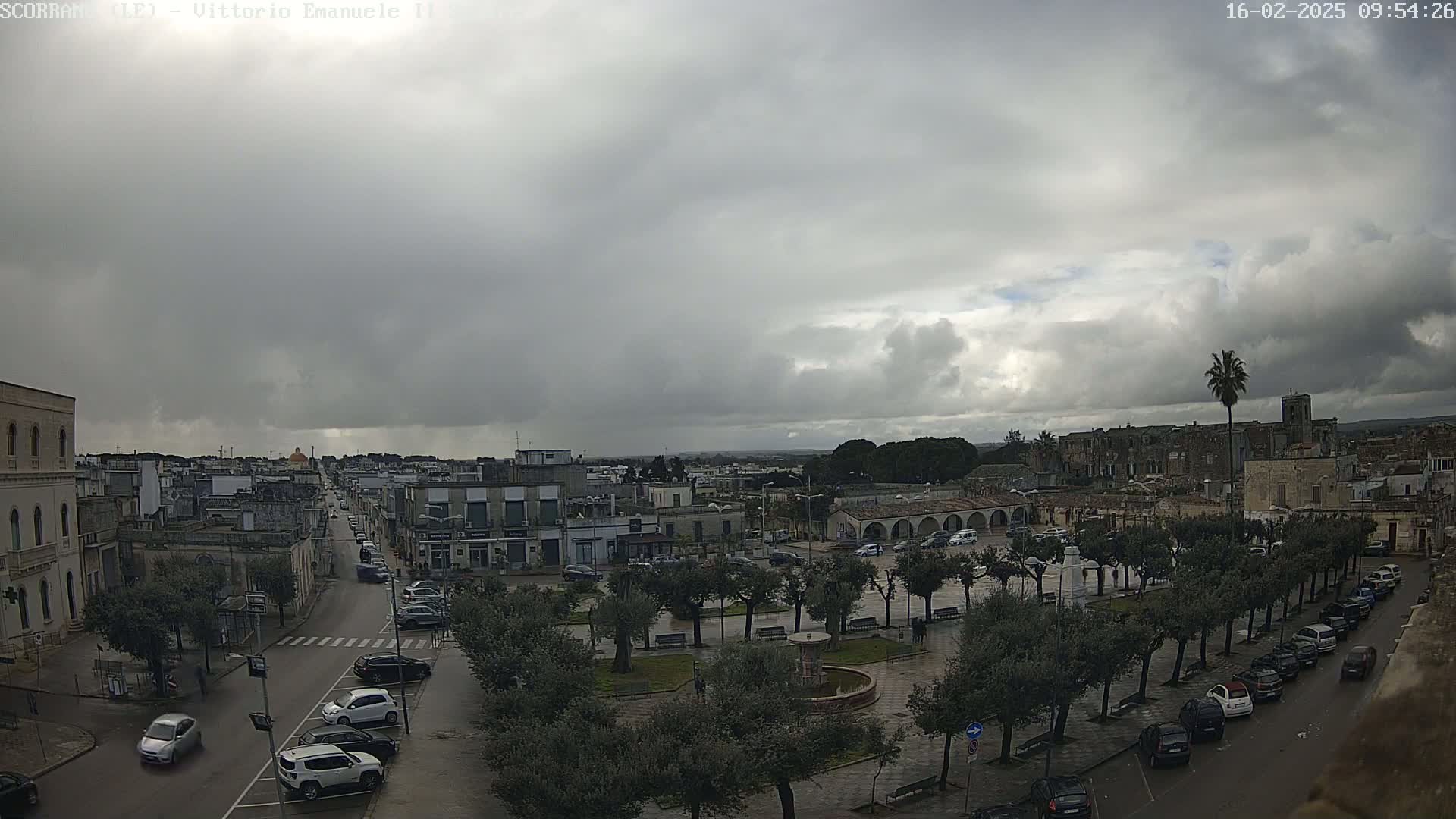 A town square with parked cars and trees under an overcast sky.