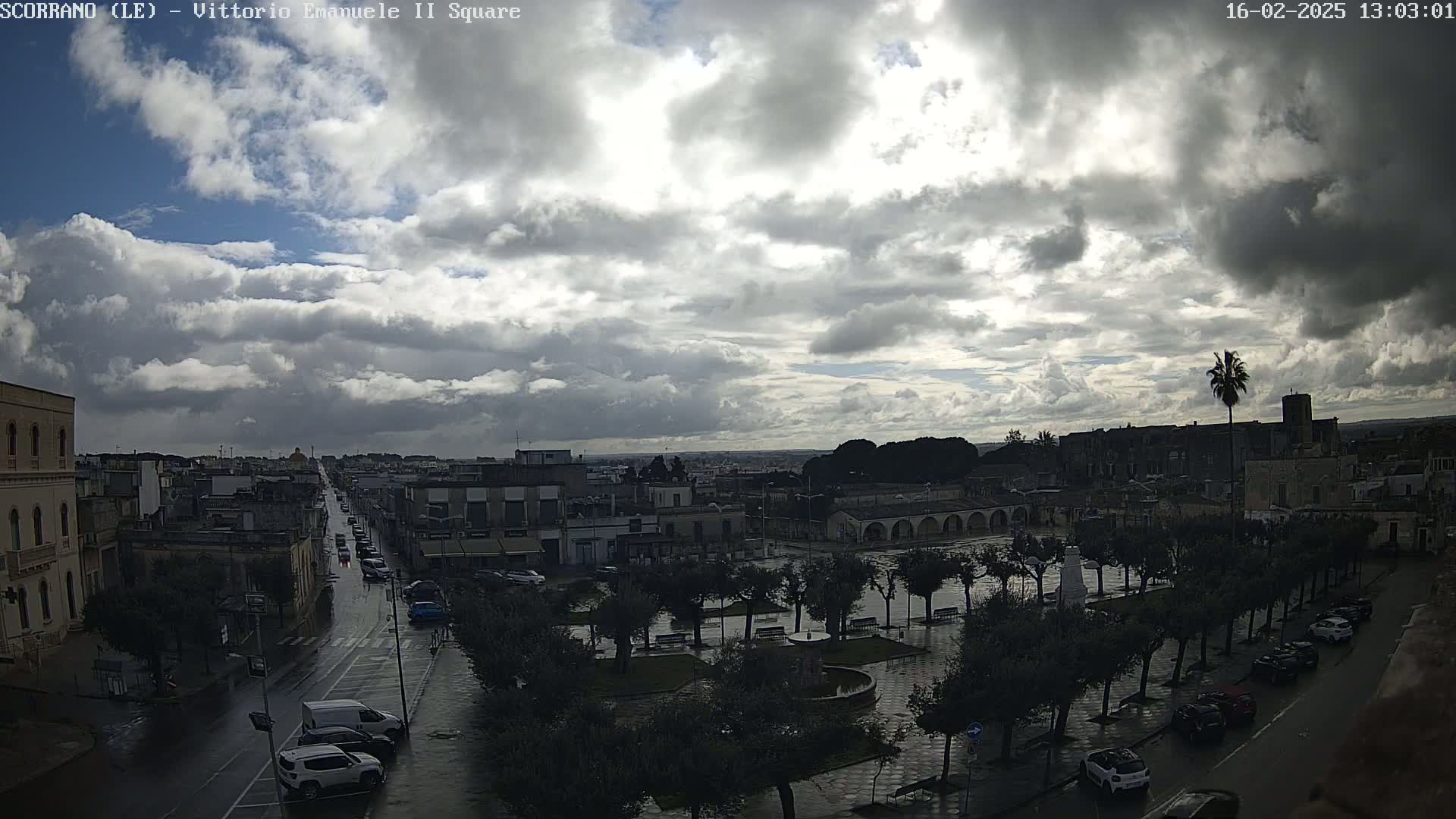 A wet town square with a long street leading to the horizon under a cloudy sky.