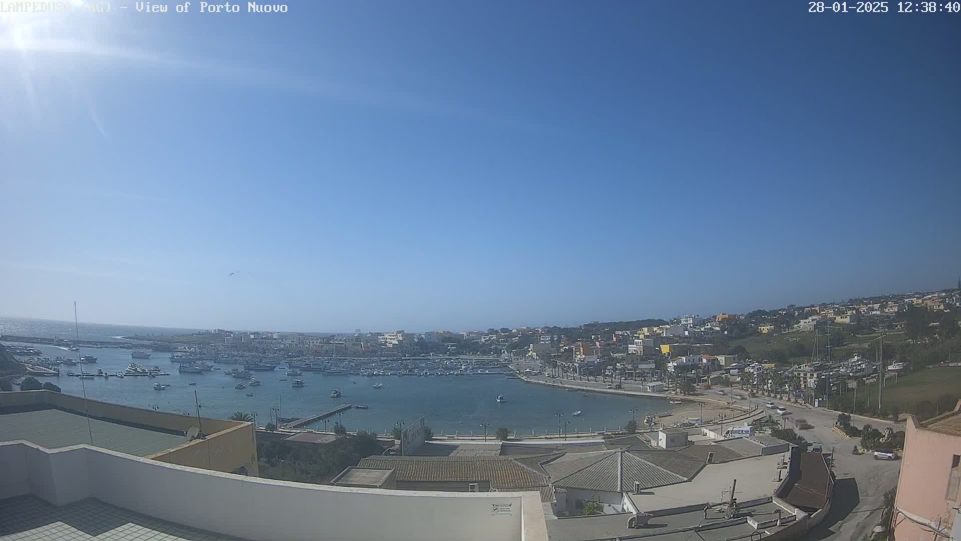 A harbor filled with boats is surrounded by a town under a clear, sunny sky.