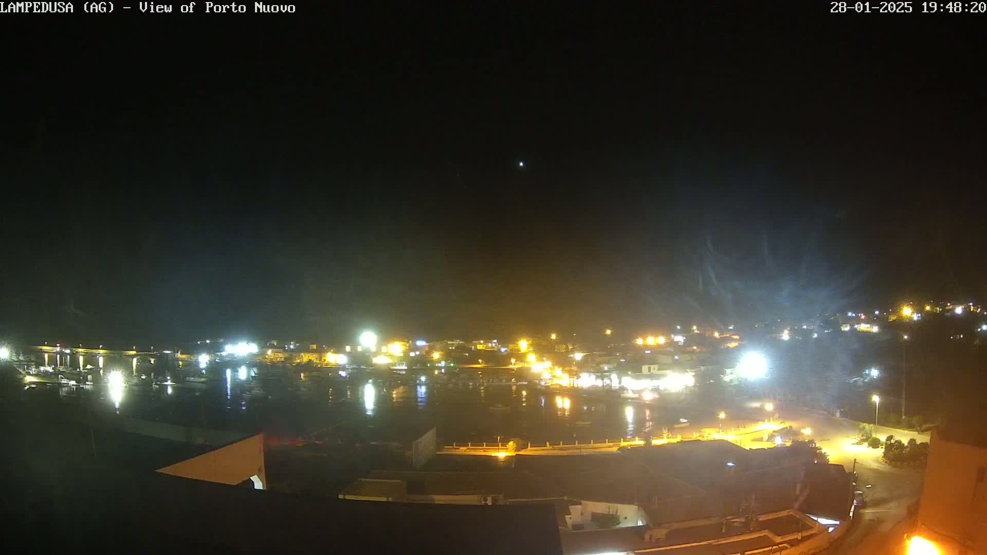 A nighttime view of a harbor town illuminated by numerous lights under a clear, dark sky.
