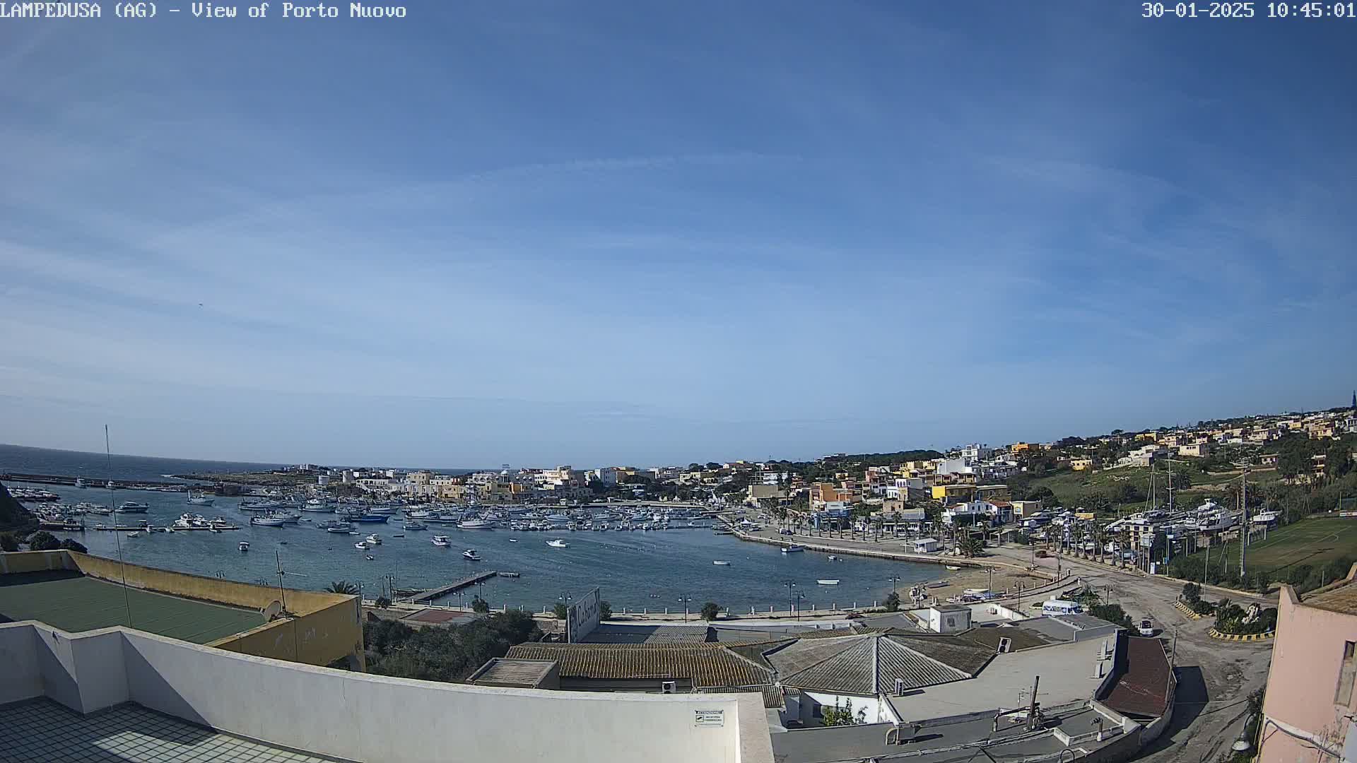 A harbor filled with boats is nestled within a town of low-rise buildings under a clear blue sky.