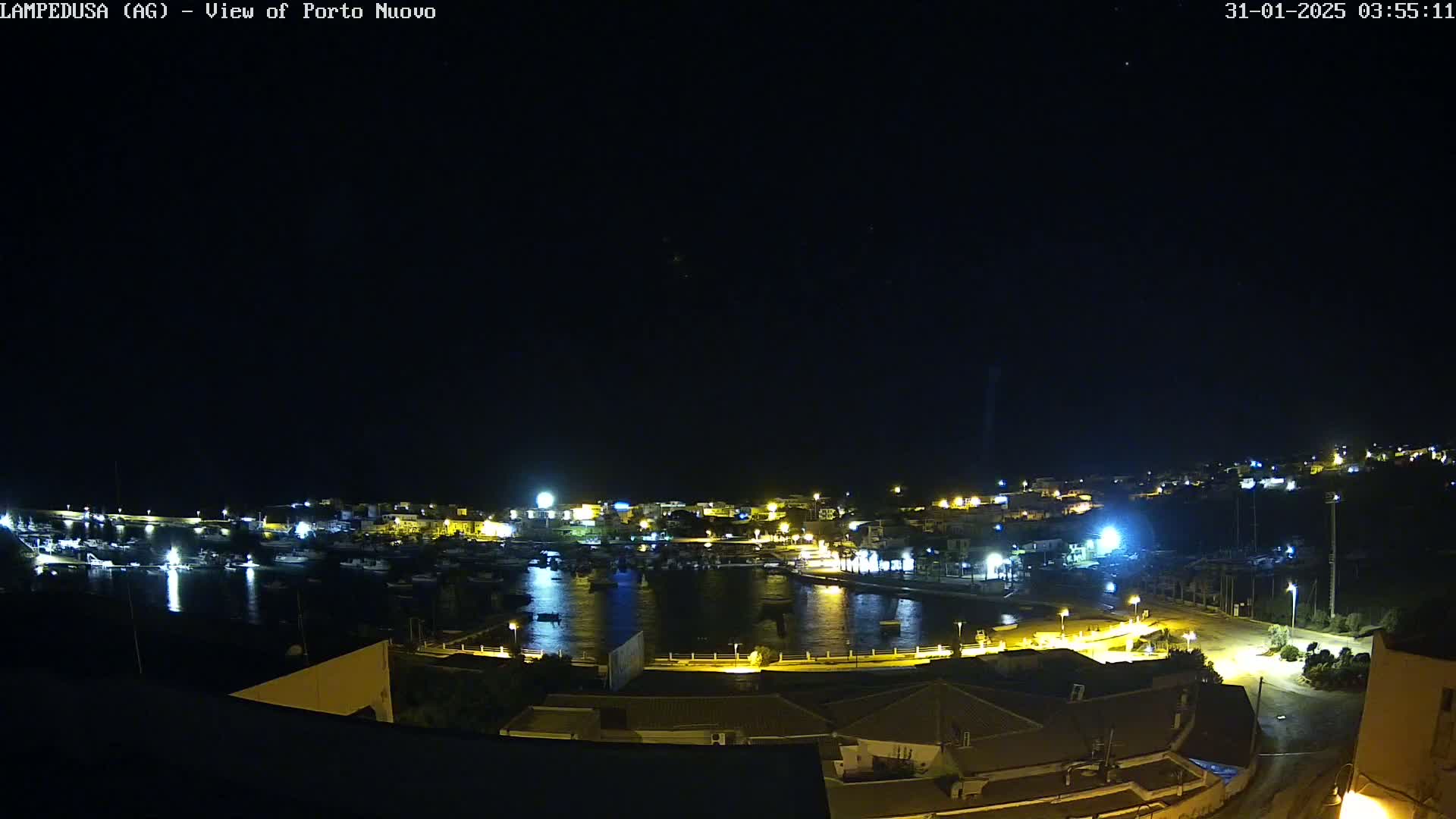 A nighttime view of a harbor town, illuminated by lights, under a clear, dark sky.