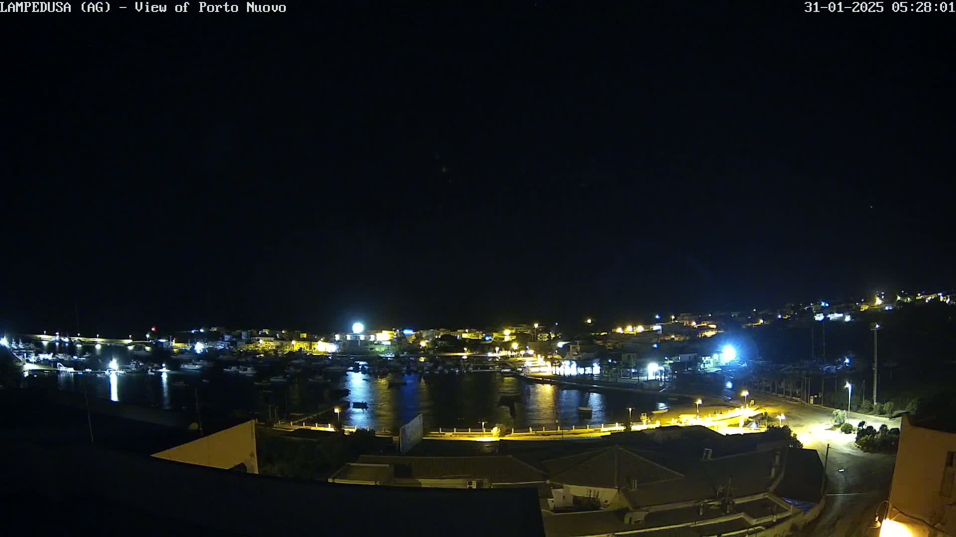 A nighttime, high-angle view of a harbor filled with boats, surrounded by illuminated buildings and a dark sky.
