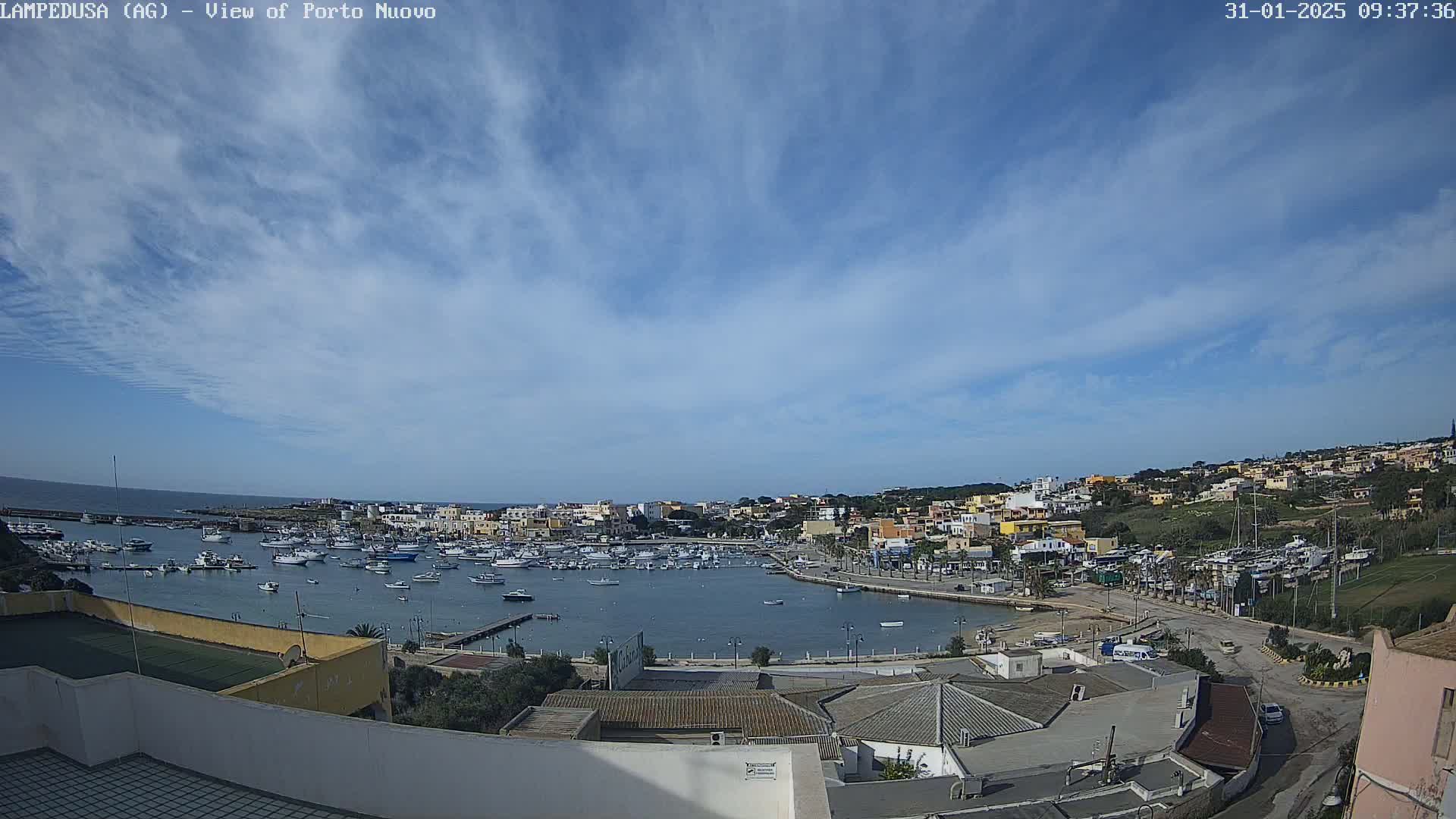 A mostly sunny day overlooks a harbor filled with boats and a town built on a hillside.