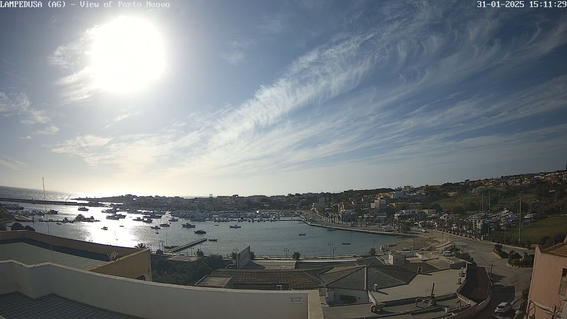 A sunny day with thin, wispy clouds over a harbor filled with boats and a town built on a hillside.