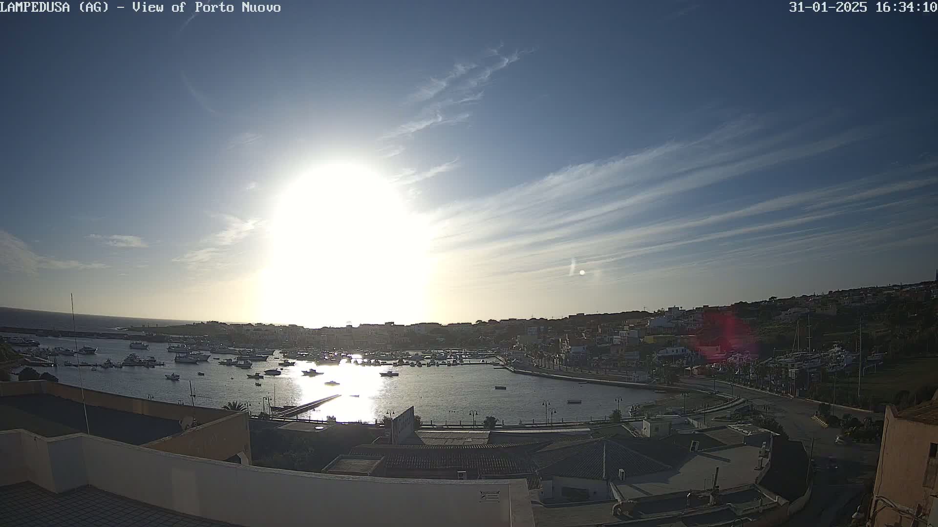 A sunny day with a few thin clouds overlooks a harbor filled with boats and a town in the background.