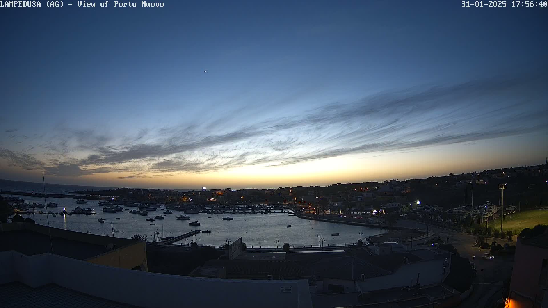 A harbor filled with boats is seen at twilight under a mostly clear sky with thin, wispy clouds.