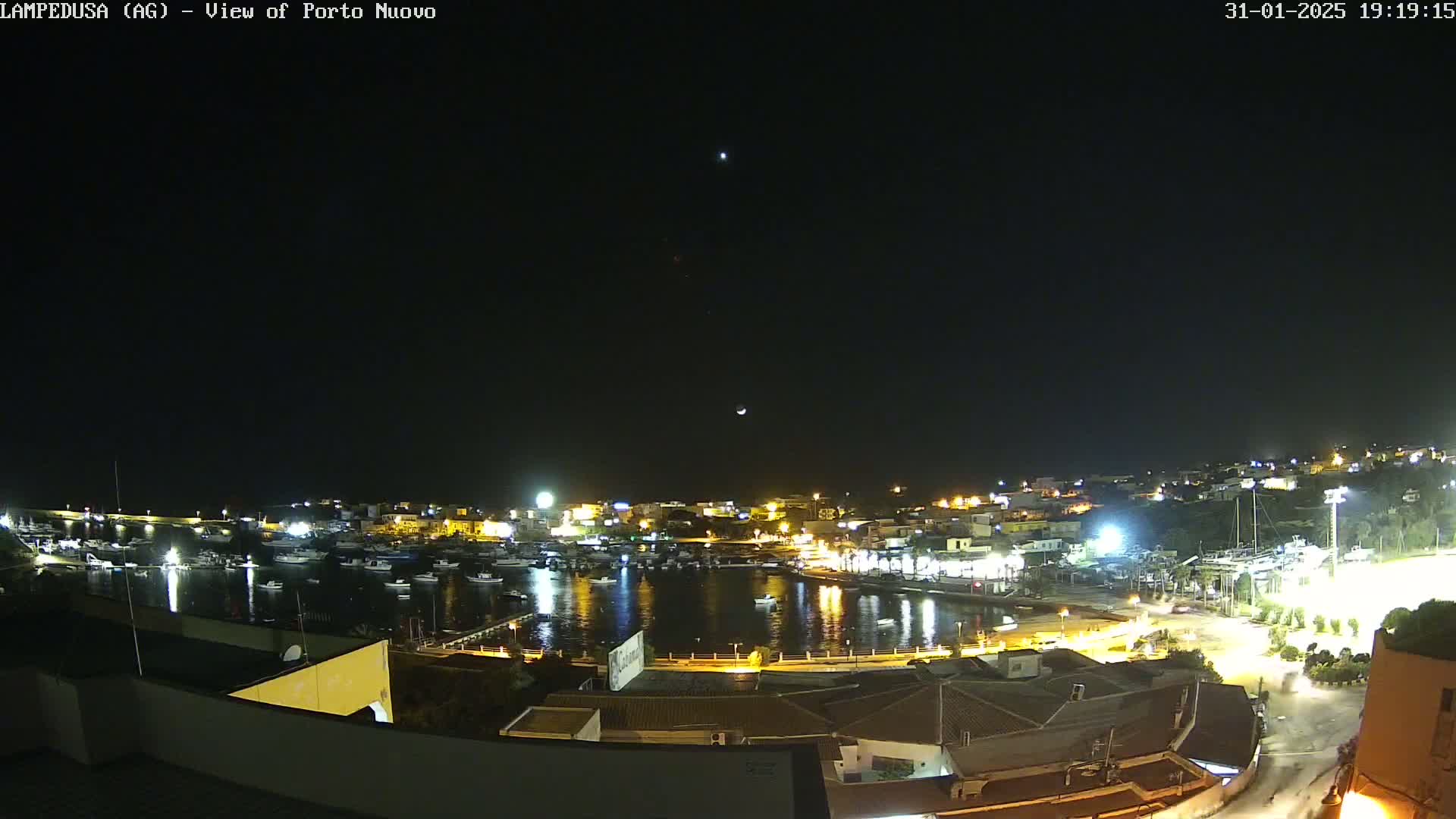 A nighttime, clear-sky view of a harbor filled with boats and illuminated buildings along the shoreline.