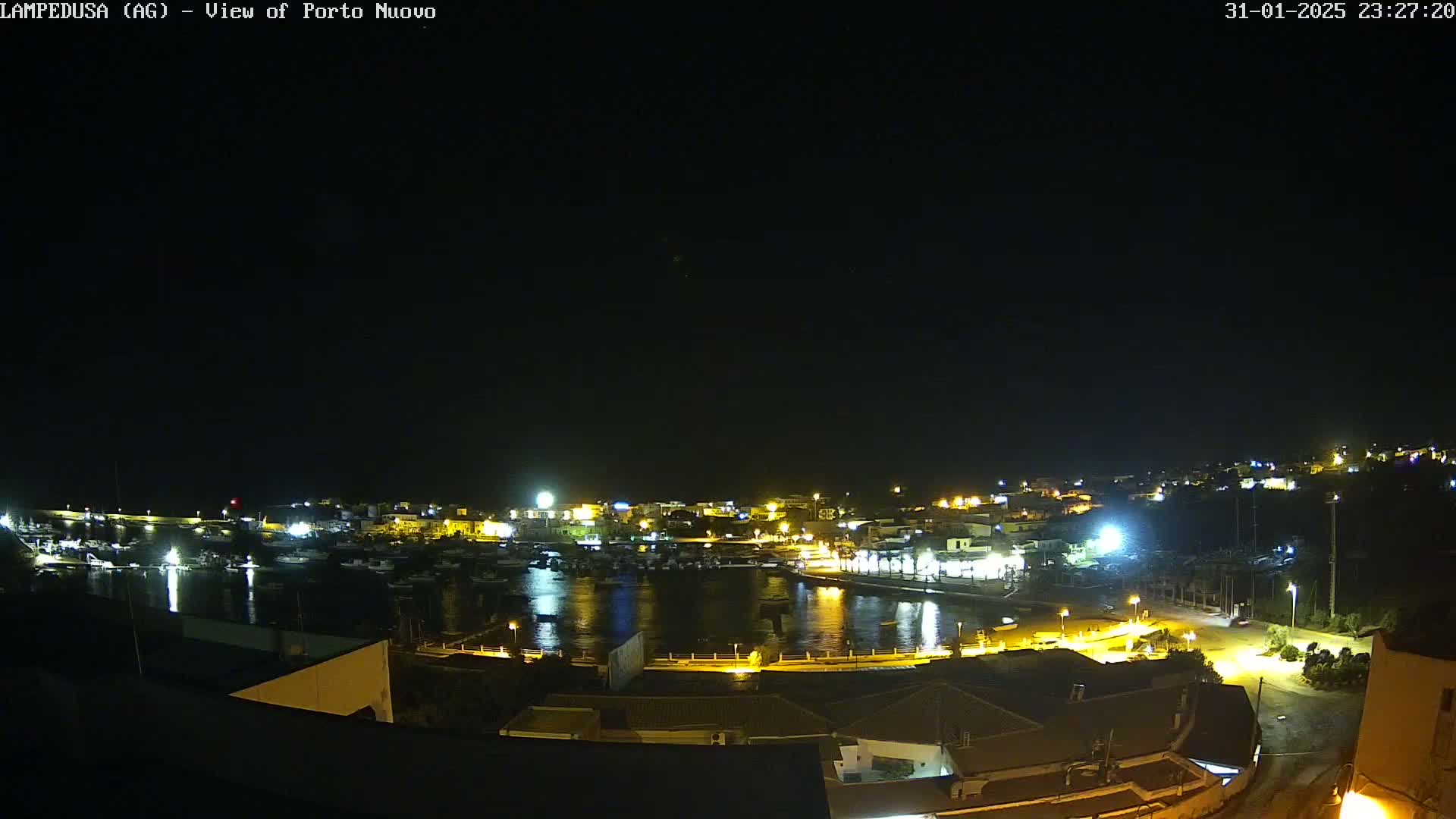 A nighttime, aerial view of a harbor town with its lights illuminating the water and buildings under a clear, dark sky.