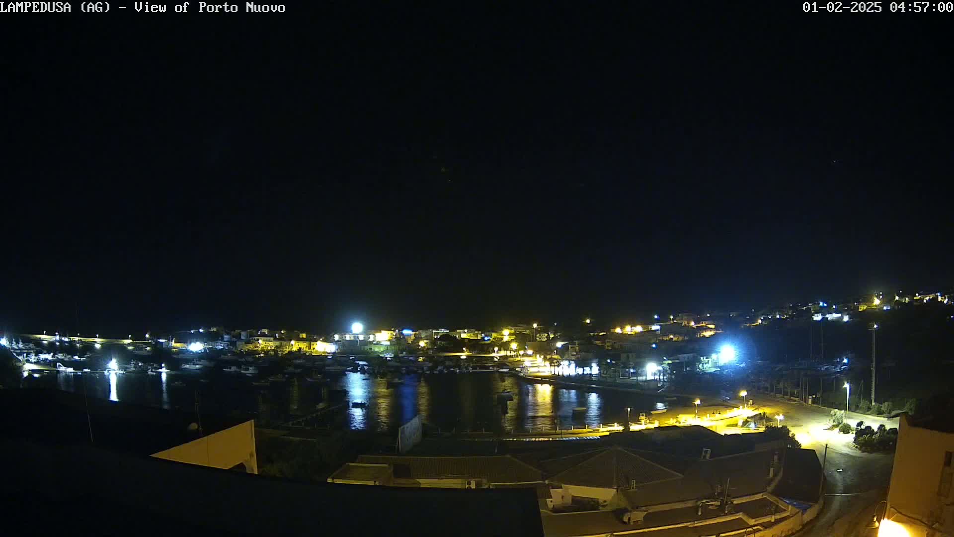 A nighttime view of a harbor with boats and illuminated buildings under a clear, dark sky.
