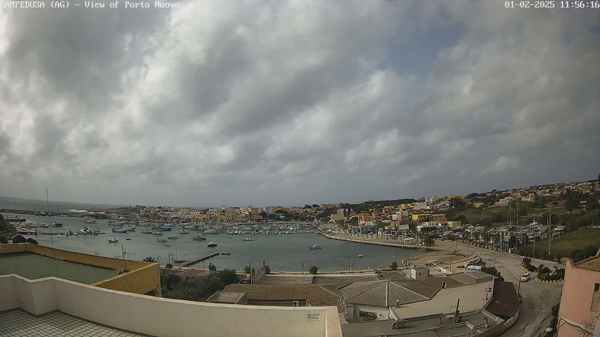 A harbor filled with boats is seen from an elevated viewpoint under a cloudy sky.