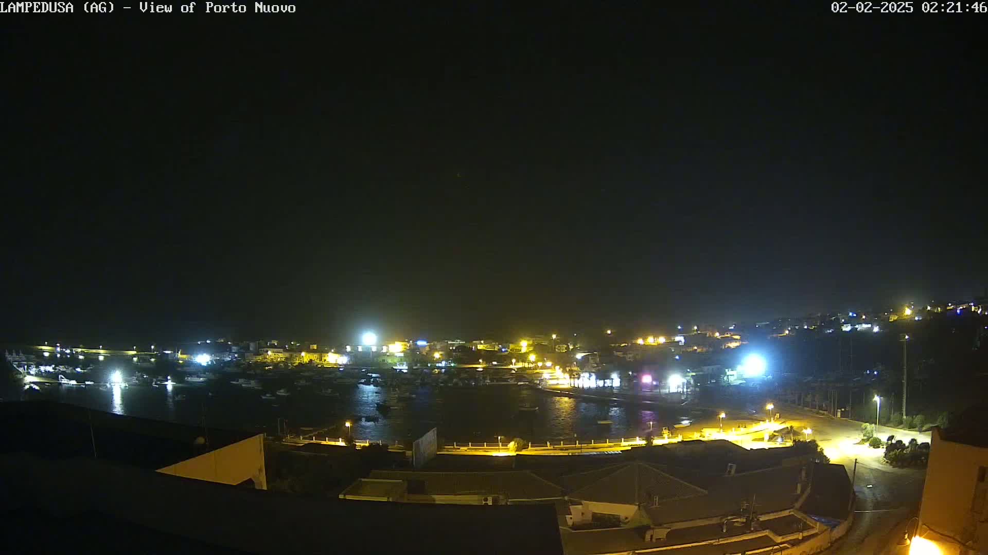 A nighttime, aerial view of a harbor filled with boats, surrounded by illuminated buildings and streets.