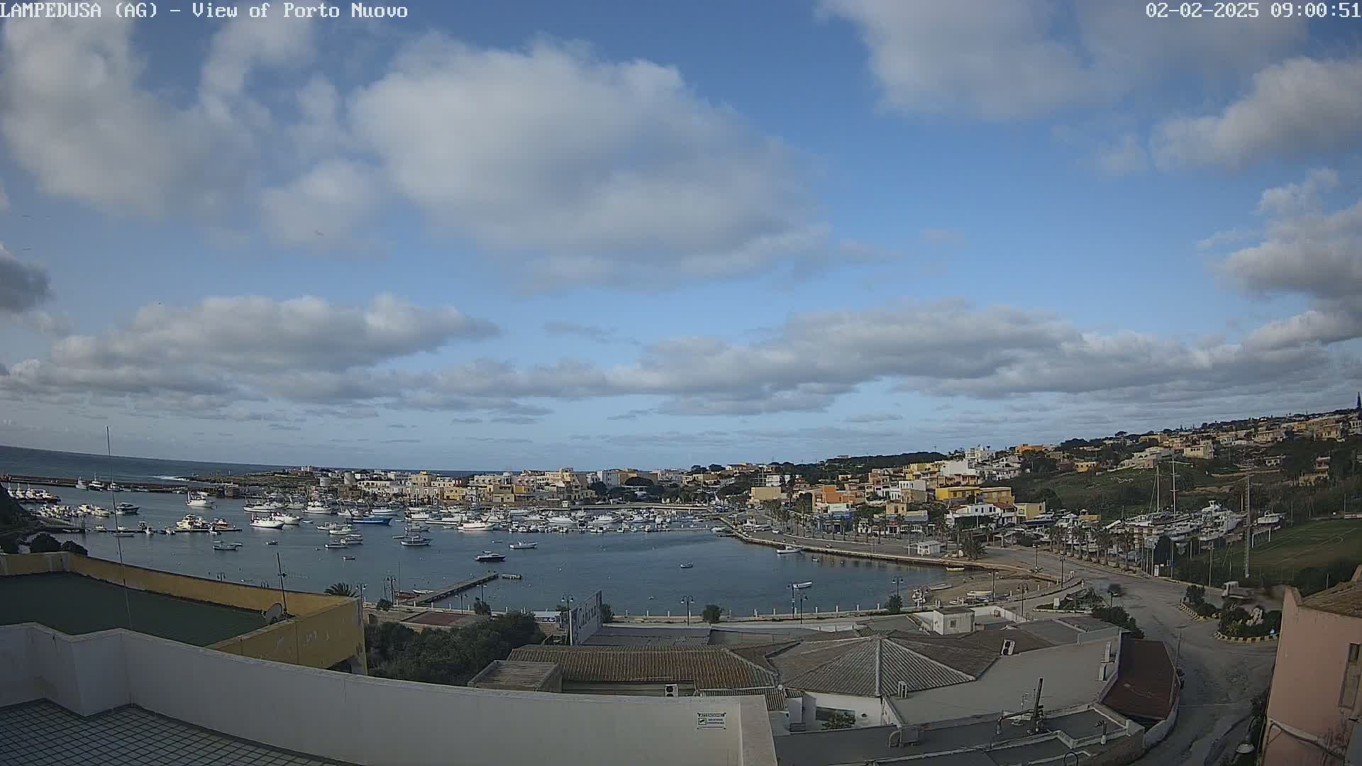 A harbor filled with boats is surrounded by a town under a partly cloudy sky.