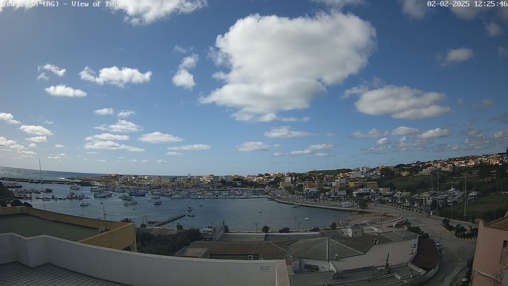A partly cloudy sky overlooks a harbor filled with boats and a town nestled on a hillside.