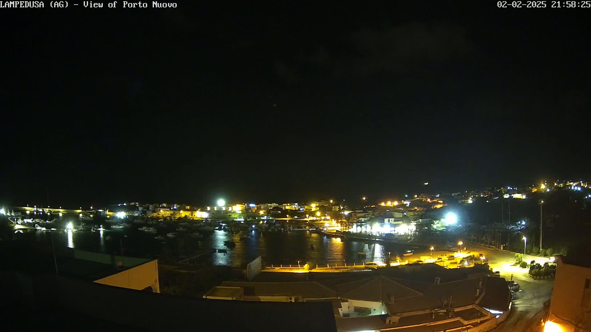 A nighttime view of a harbor town, illuminated by lights, under a dark, cloudy sky.
