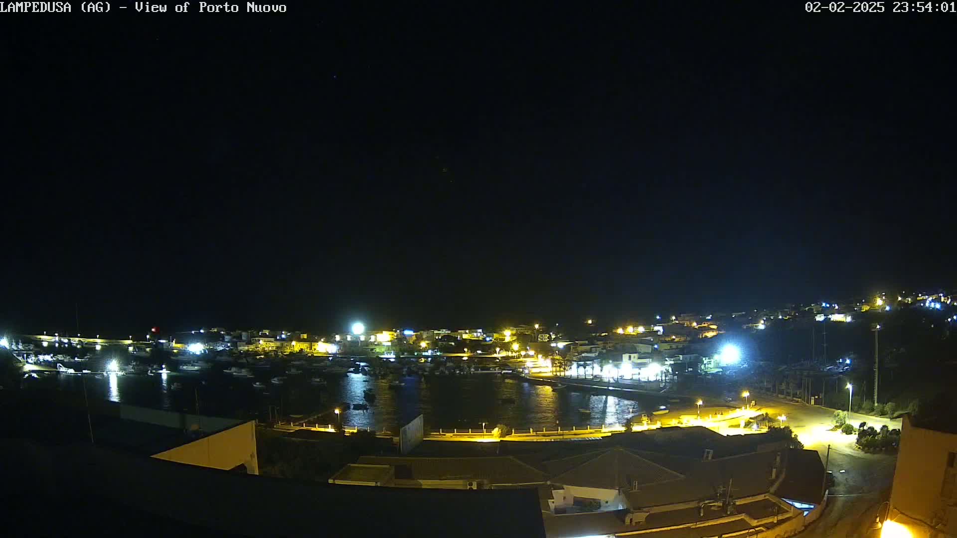 A nighttime, high-angle view of a harbor town with its lights illuminated against a clear, dark sky.
