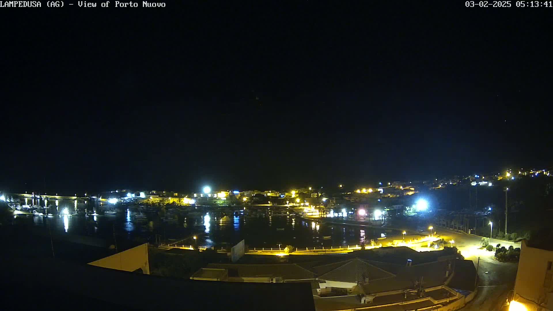 A nighttime view of a harbor filled with boats, surrounded by illuminated buildings and streets under a clear, dark sky.