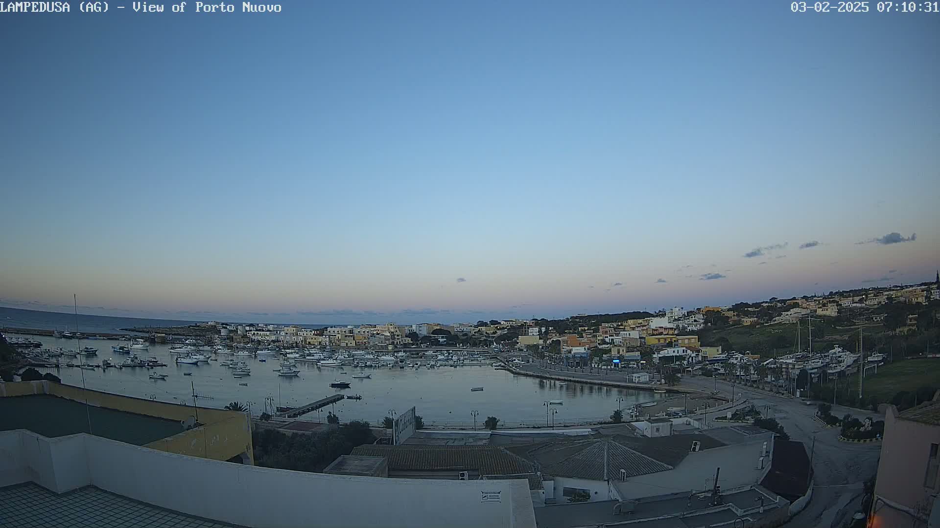 A harbor filled with numerous boats is situated in a town under a twilight sky with a few clouds.