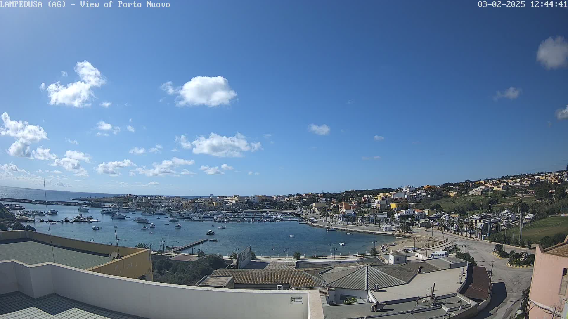 A mostly sunny day overlooking a harbor filled with boats and a town nestled on a hillside.