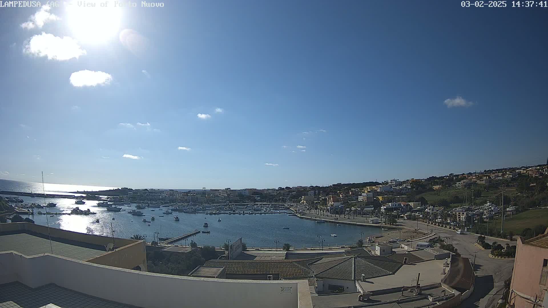 A sunny day reveals a harbor filled with boats, surrounded by a town nestled against a hillside under a mostly clear blue sky.