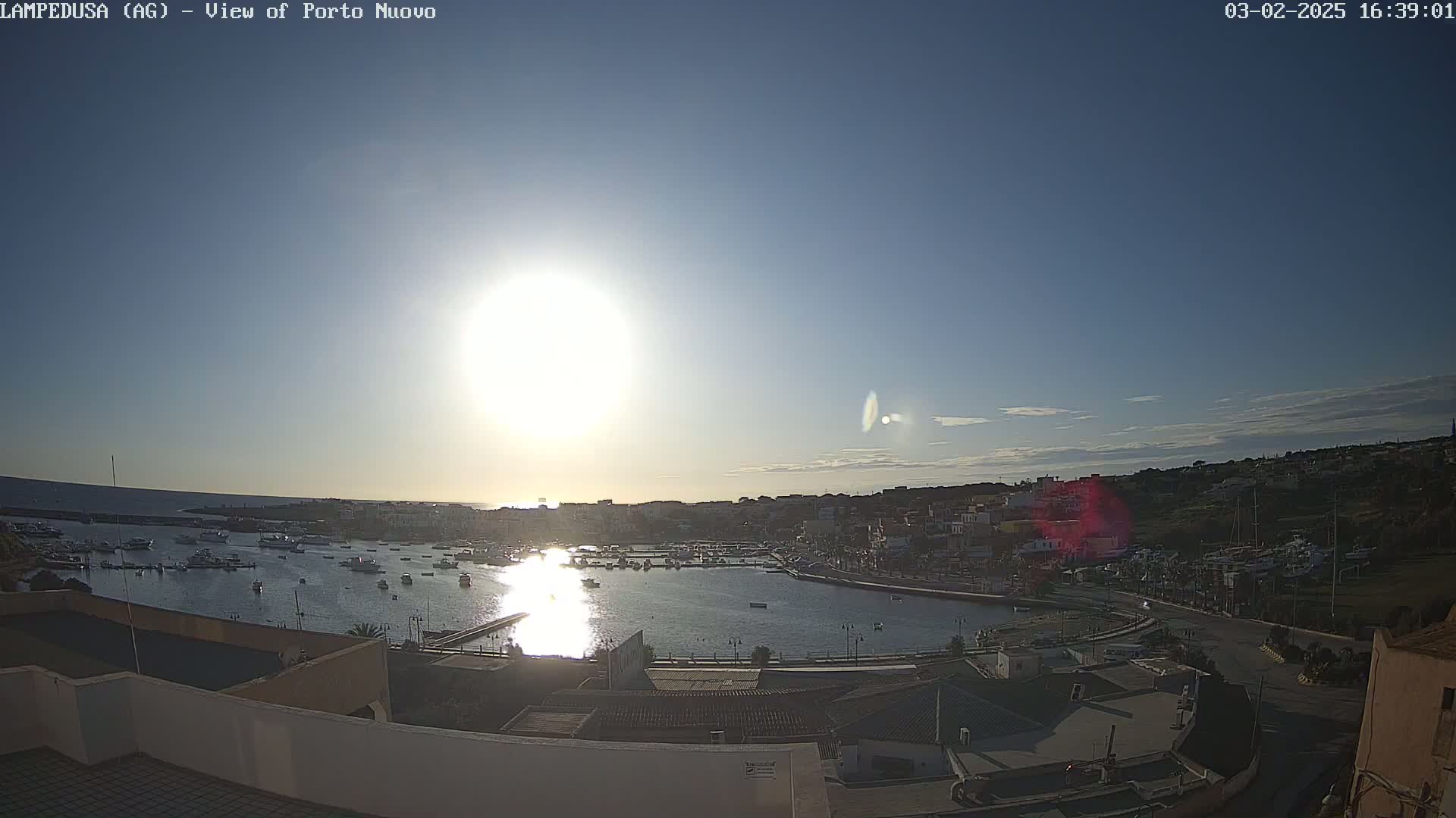 A sunny day shows a harbor filled with boats, a town, and buildings along the waterfront.