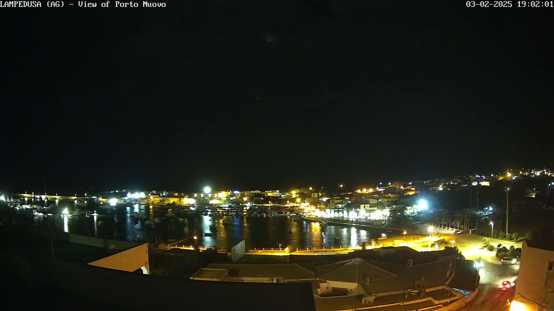 A nighttime, high-angle view of a brightly lit harbor town with boats in the water under a clear, dark sky.