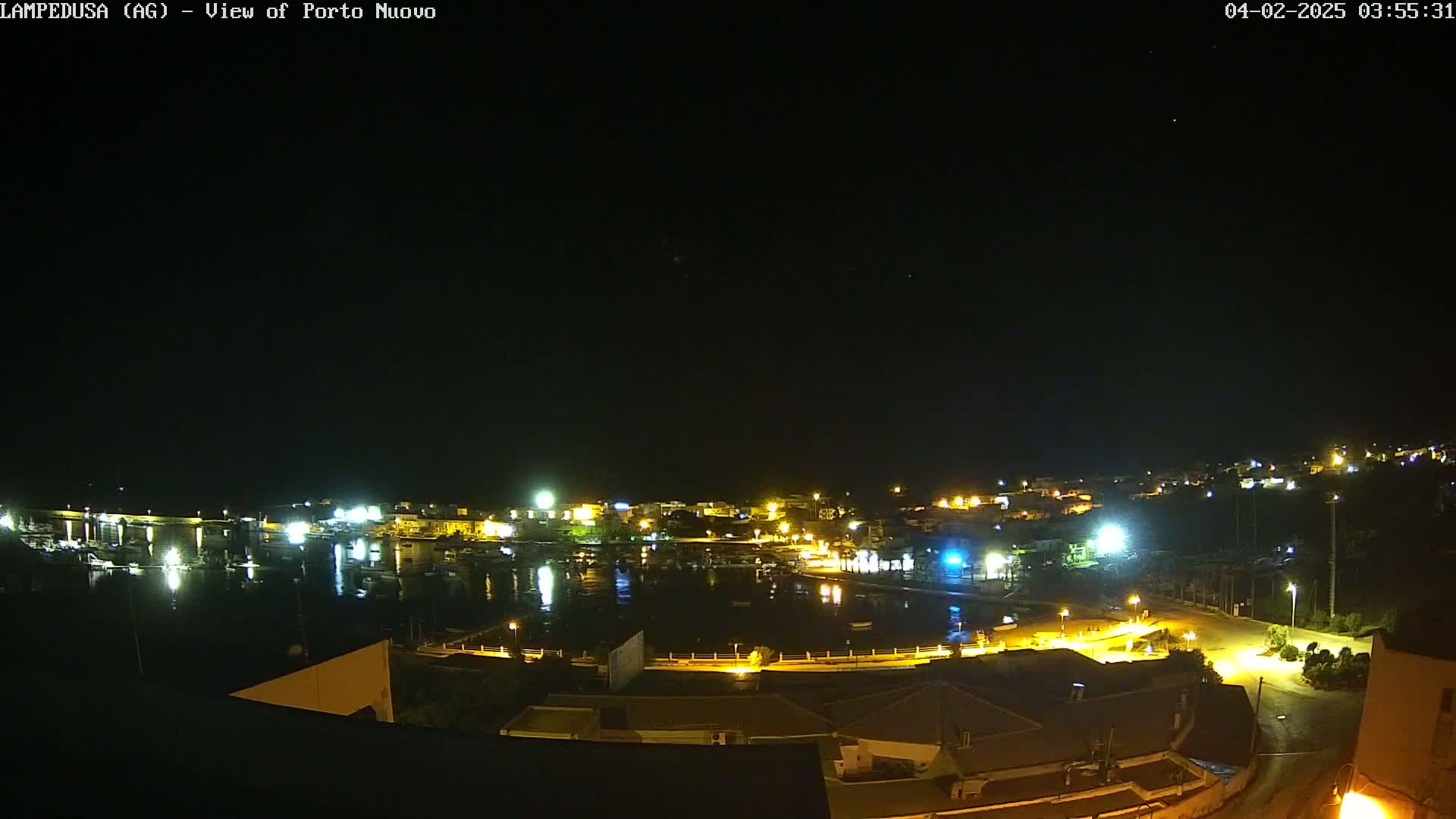 A nighttime view of a harbor town's illuminated waterfront and buildings under a clear, dark sky.