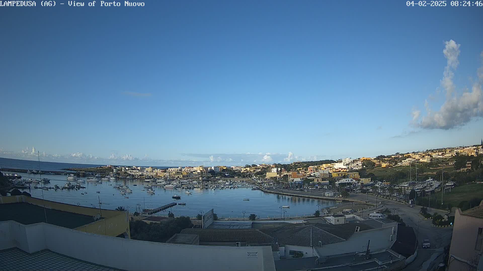 A mostly clear blue sky overlooks a harbor filled with boats and surrounded by a town of low-rise buildings.