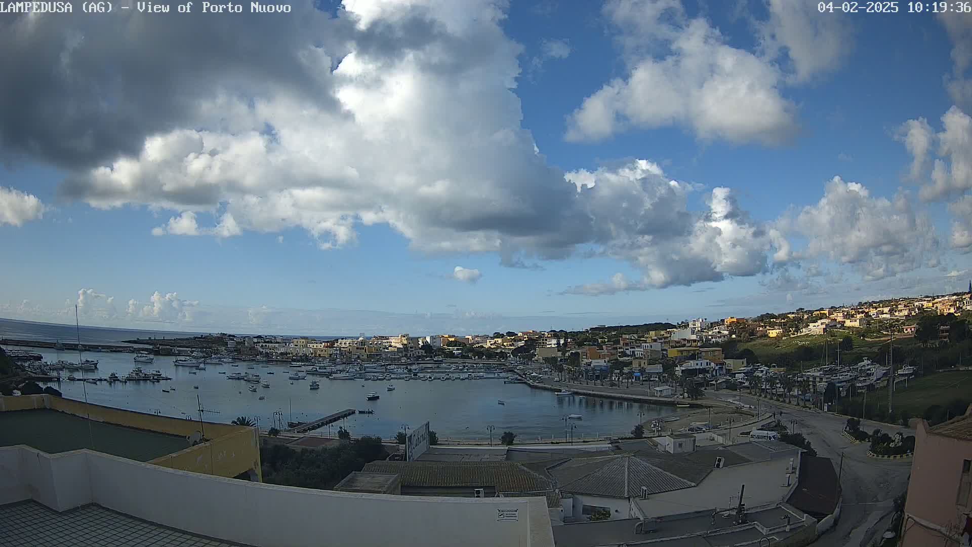 A partly cloudy day overlooks a harbor filled with boats and a town built on a hillside.