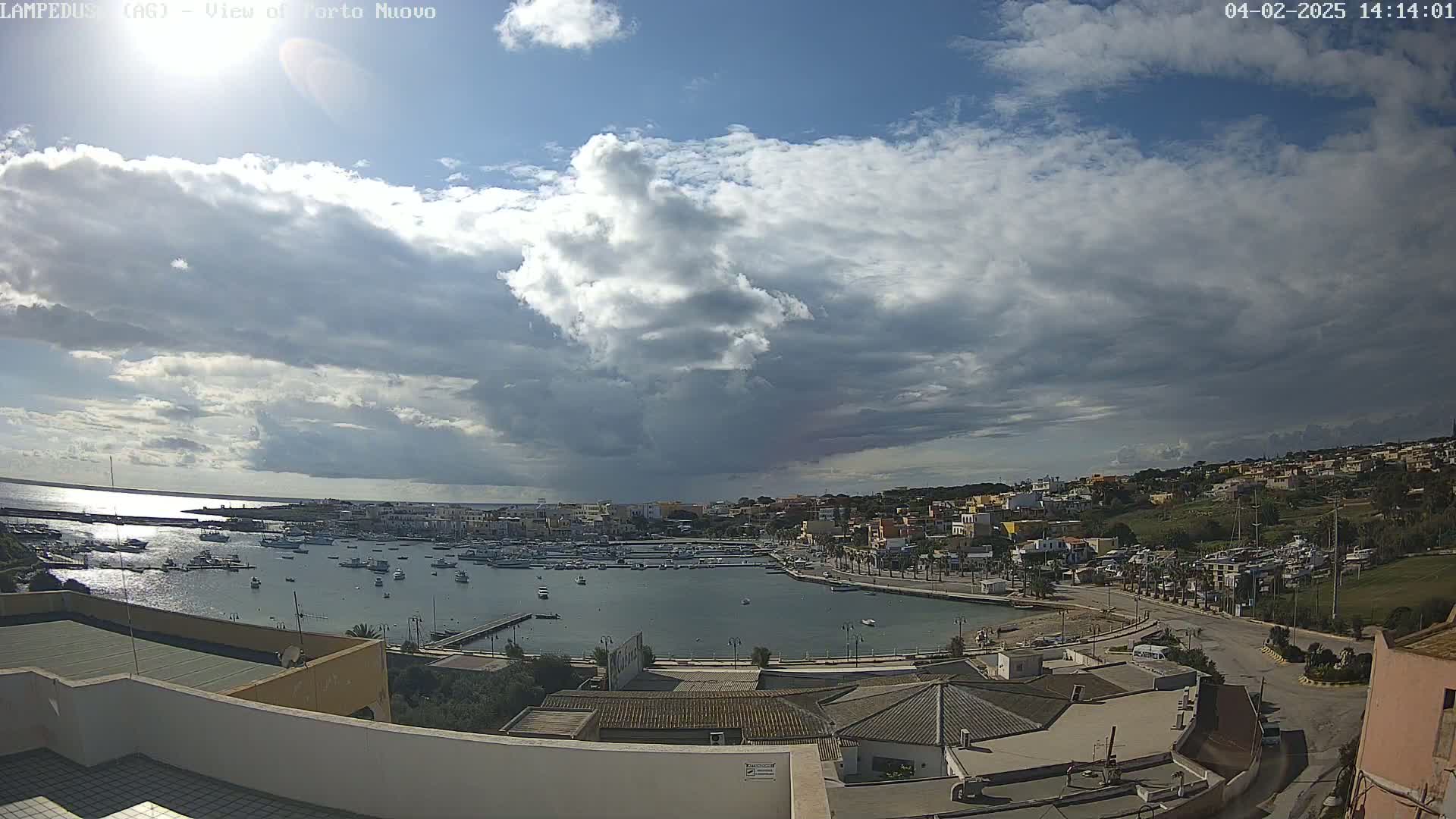 A partly cloudy sky overlooks a harbor filled with boats and a town nestled on a hillside.
