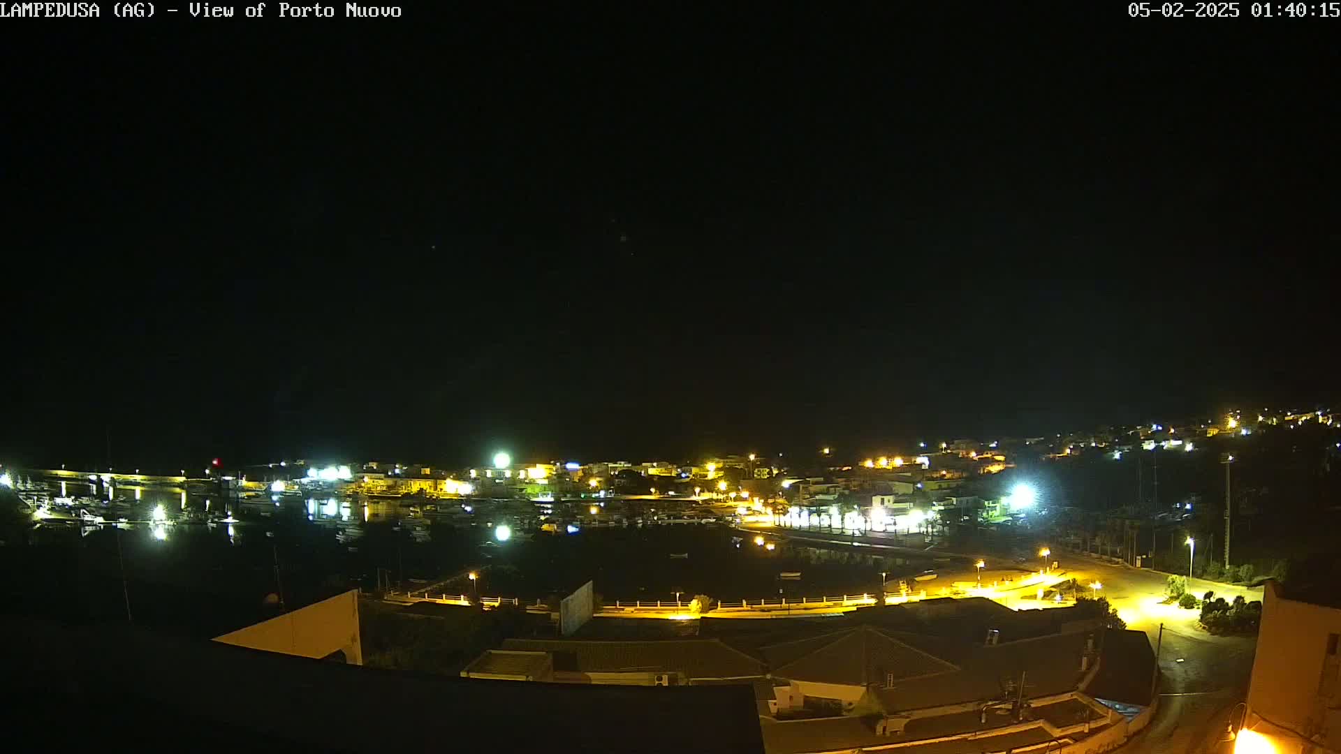 A nighttime aerial view of a harbor town, illuminated by streetlights and building lights under a clear, dark sky.