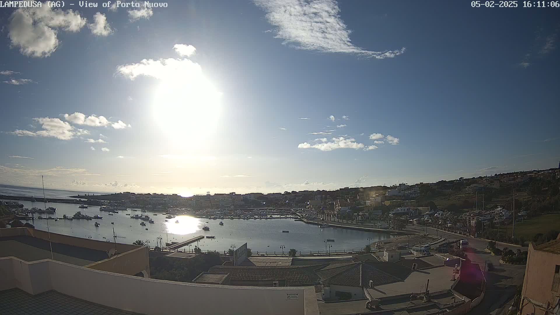 A sunny day with scattered clouds over a harbor filled with boats, next to a town built on a hillside.