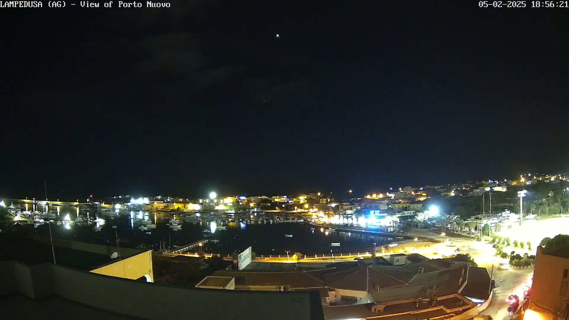 A nighttime, clear-sky view of a harbor town with boats in the water and illuminated buildings along the shoreline.