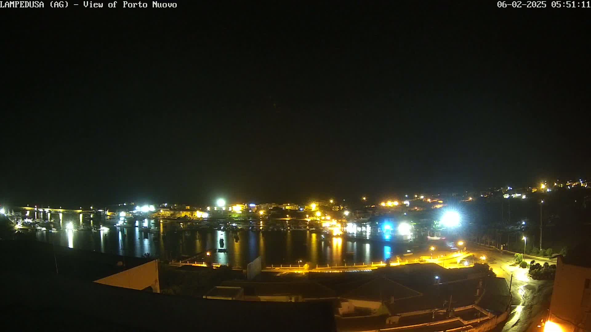 A nighttime, high-angle view of a harbor town with its lights reflecting on the calm water.