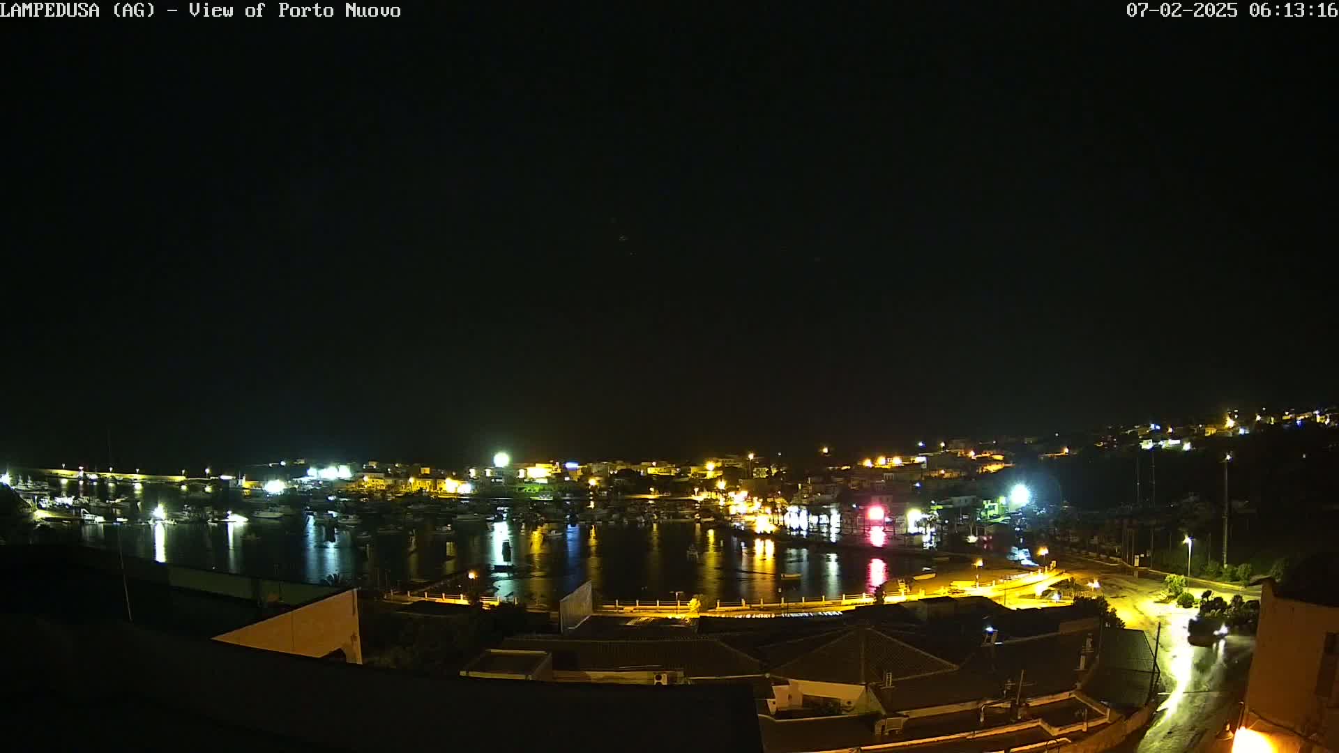 A nighttime, overhead view of a harbor filled with boats, surrounded by illuminated buildings and streets, under a clear, dark sky.