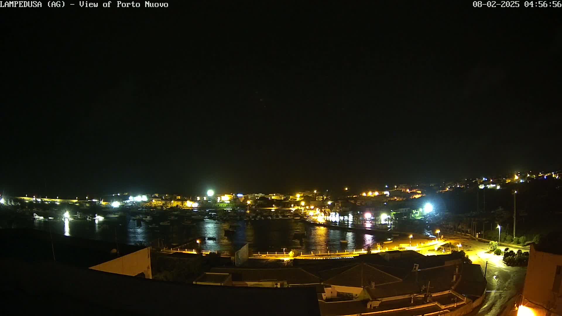 A nighttime, high-angle view of a harbor town with boats in the water and buildings lit up along the shoreline.