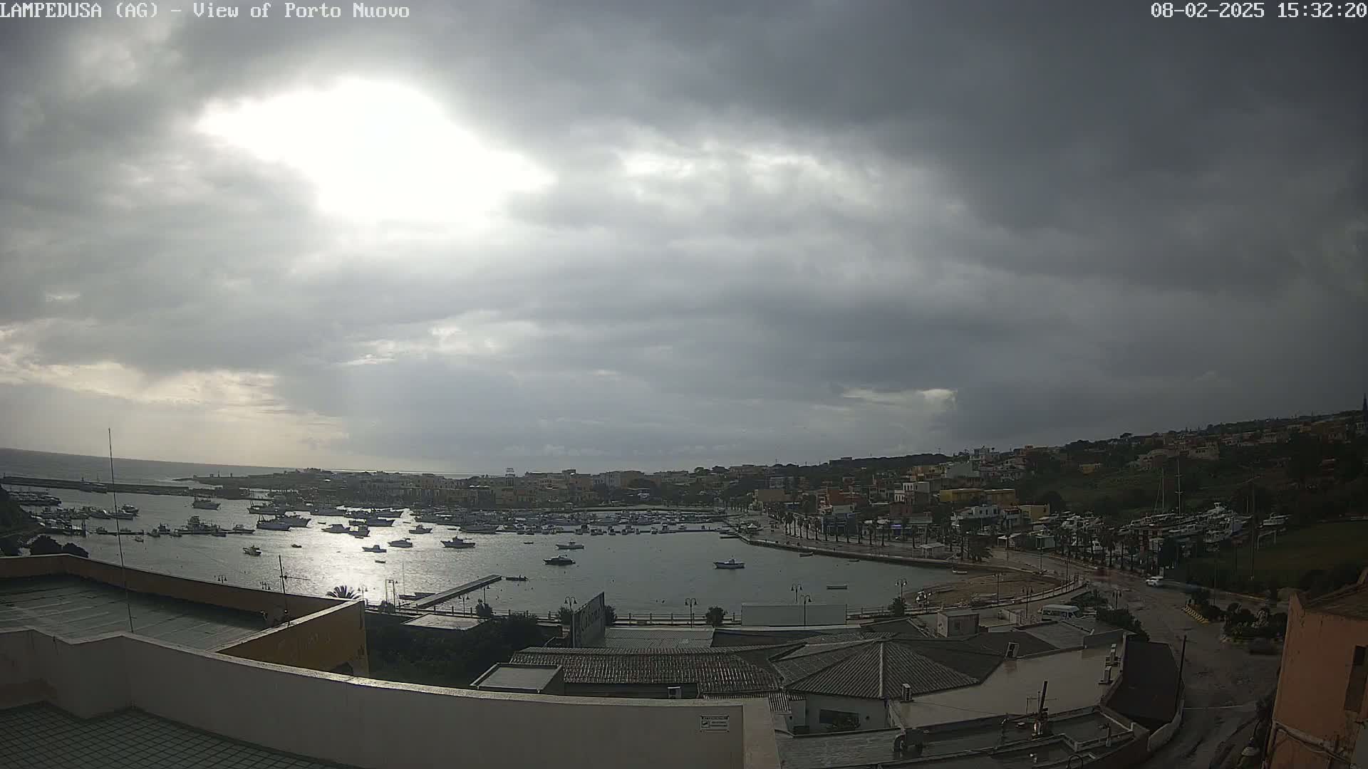 An overcast sky hangs over a harbor filled with numerous boats, adjacent to a town with low-rise buildings.