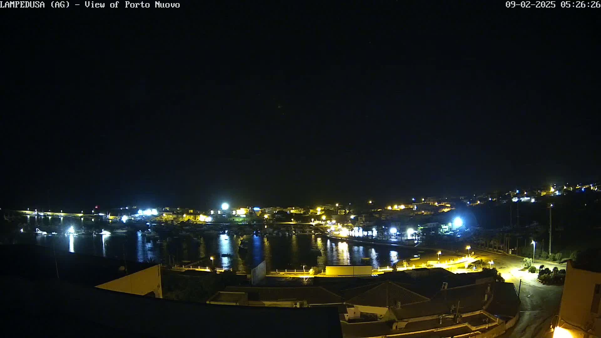 A nighttime, high-angle view of a harbor town with boats in the water and lights illuminating buildings and streets.
