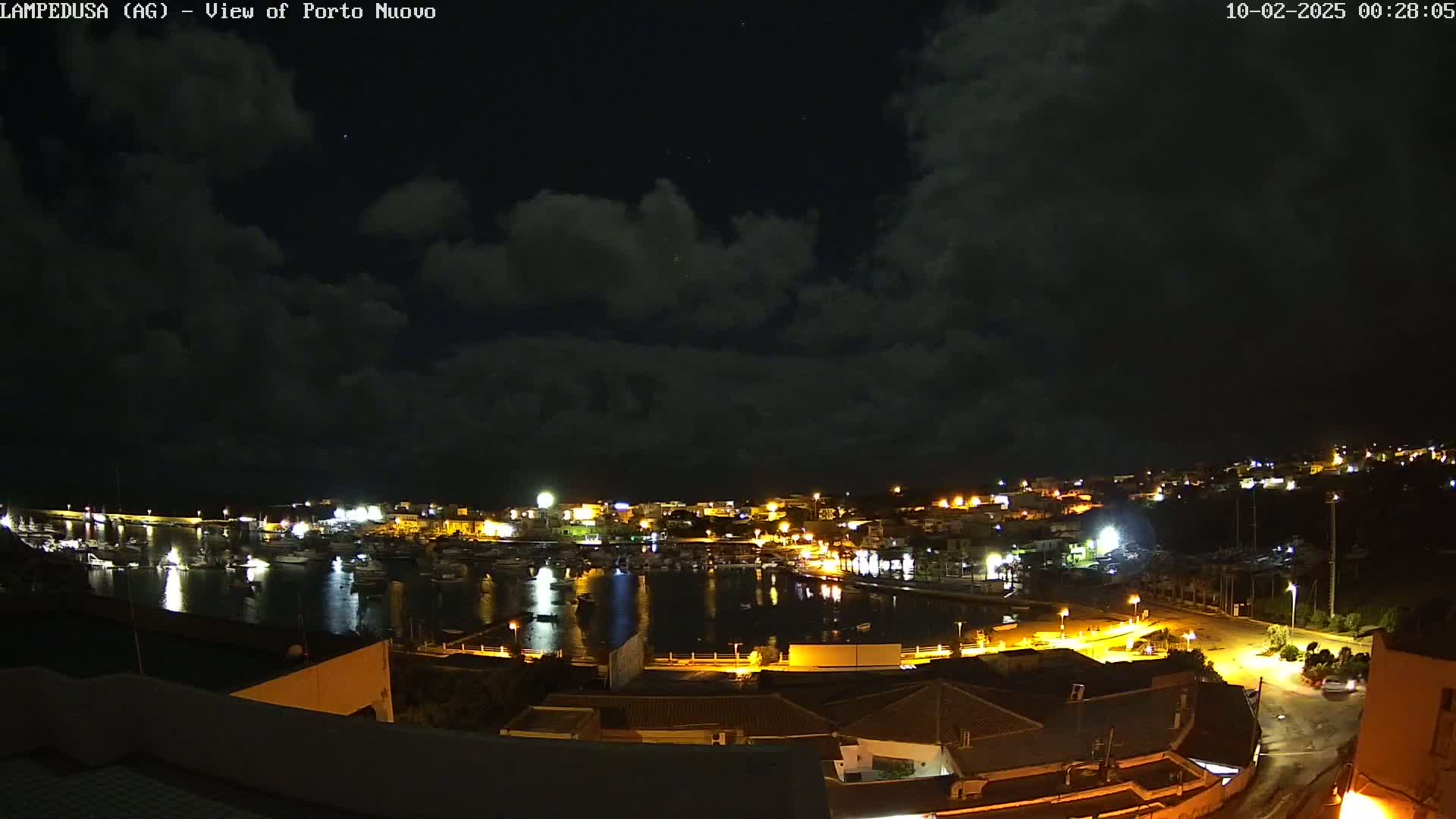 A nighttime view of a harbor town with many boats in the water under a partly cloudy sky.