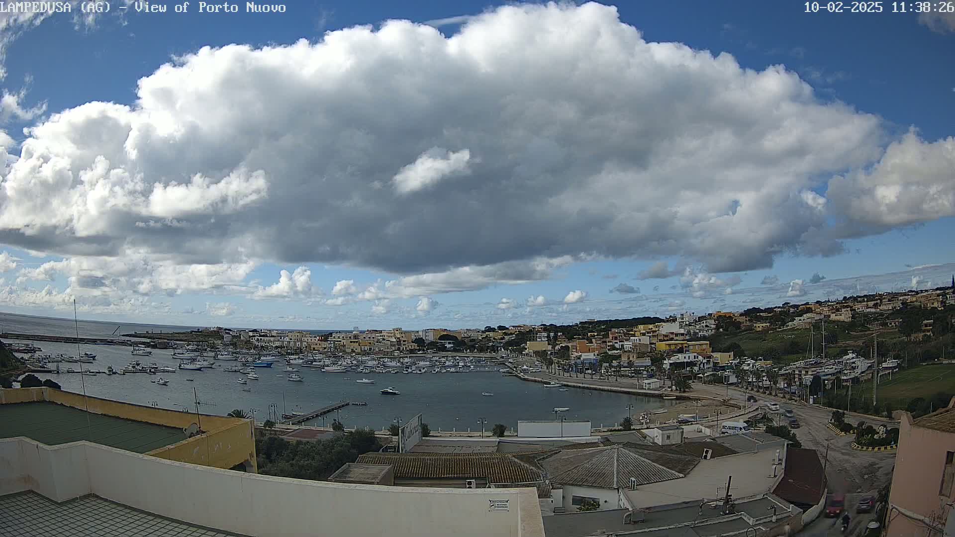 A partly cloudy day overlooks a harbor filled with boats and a town nestled on a hillside.