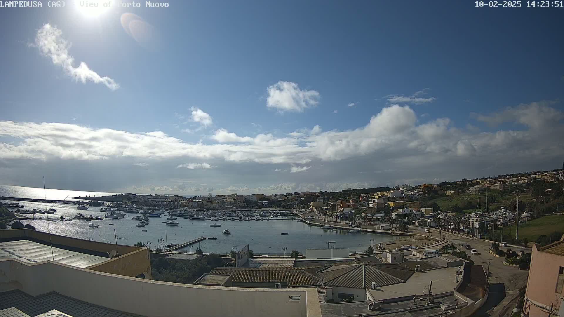 A partly cloudy sunny day overlooks a harbor filled with boats and a town built on a hillside.